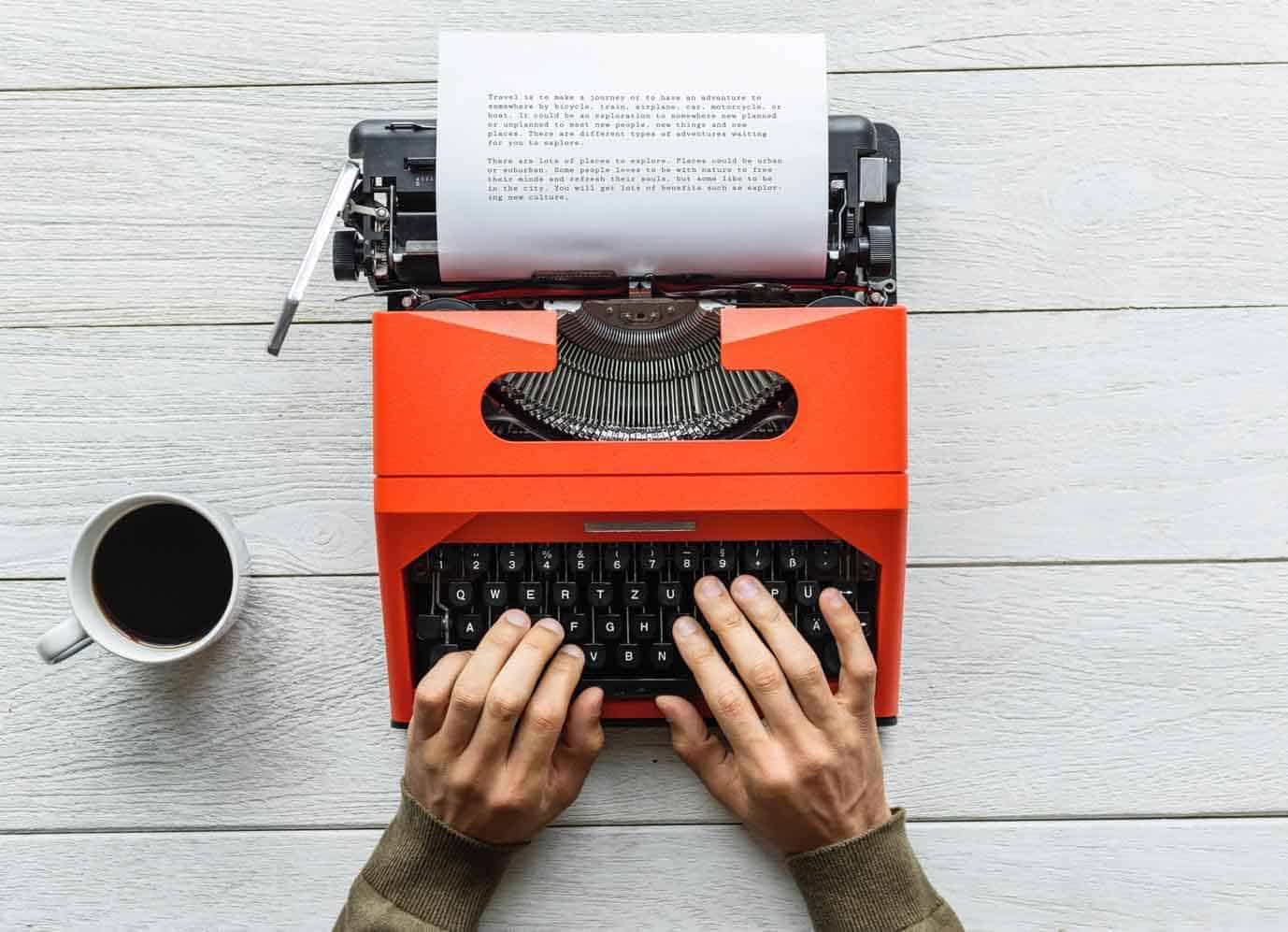 a person typing on his typewriter with a glass of coffee beside him