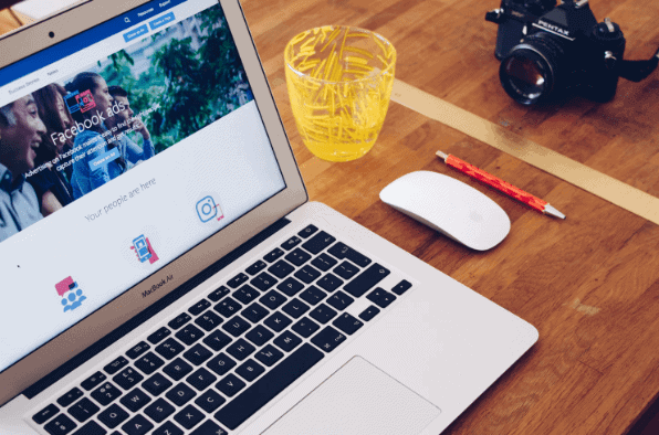 A laptop with Facebook Ads support on the screen with magic mouse, pen and cup on the right side