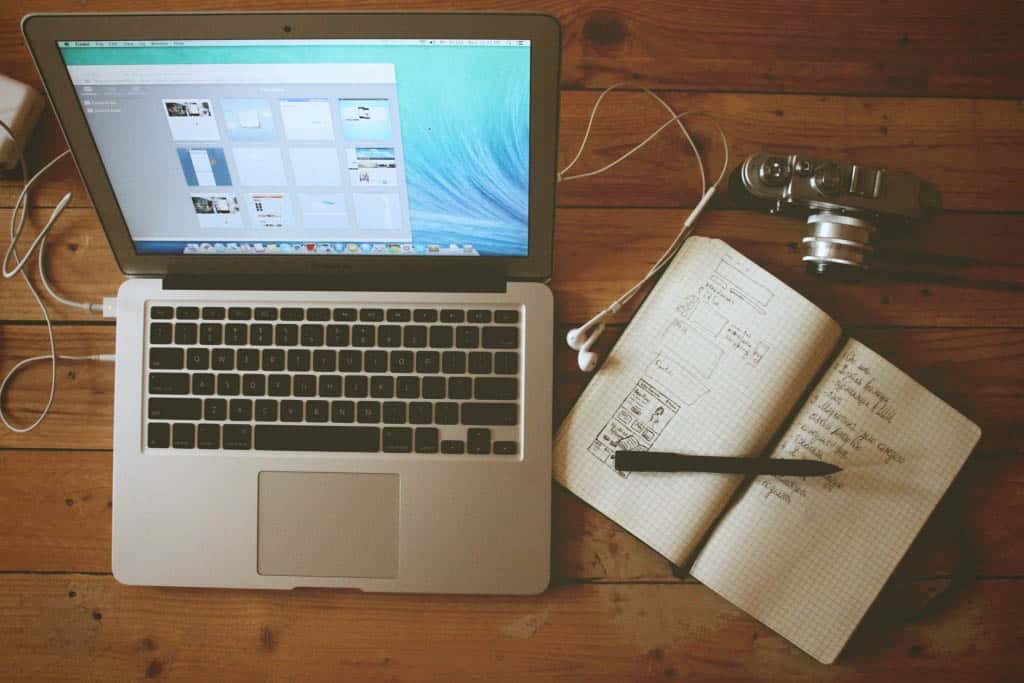 An open macbook with earphone plugged in and a planner and camera on its right side